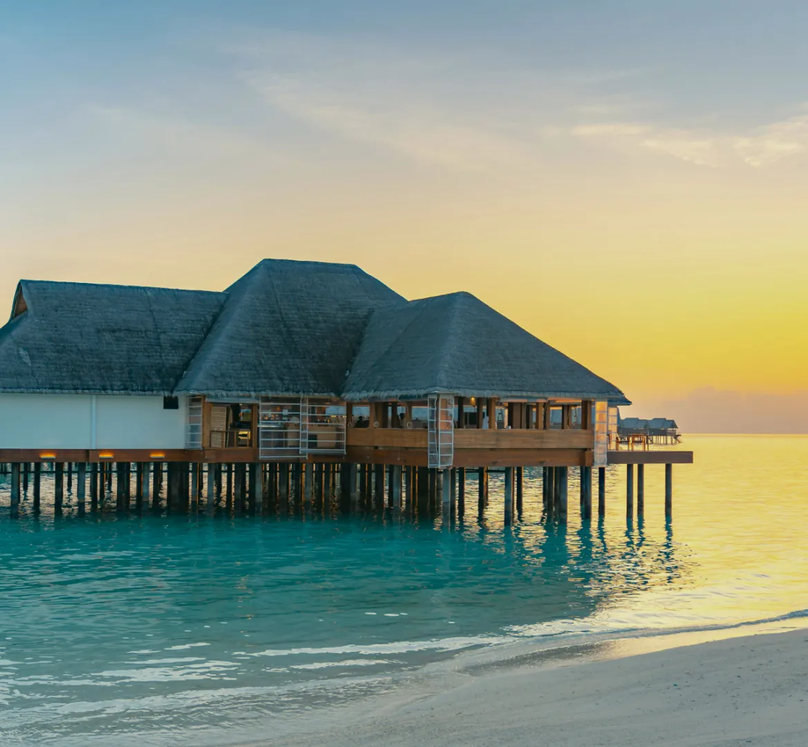 A beautiful house build out off the shore of the ocean with a colorful sunset in the background.